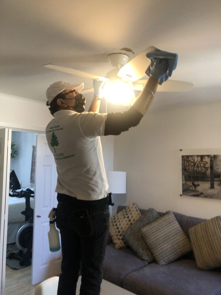 A man cleaning the fan of a house with a cloth